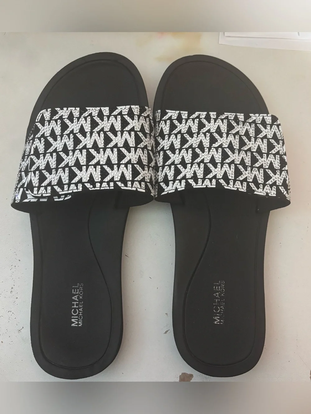 Michael Kors black & white slides featuring a signature logo print on the strap.